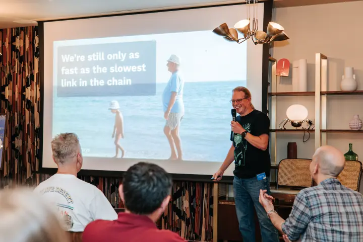 A speaker presenting beside a projected slide at the July gathering