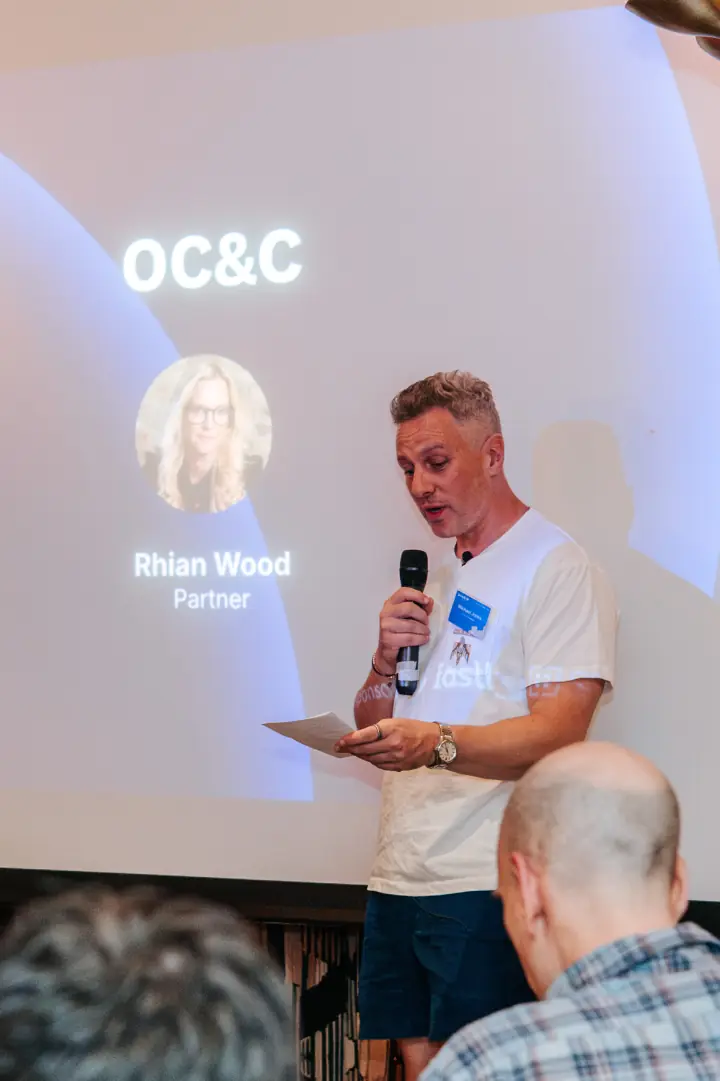 A speaker holding a microphone in front of the OC&C presentation