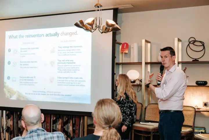 A speaker discussing how organisations are changing with AI, beside a projected presentation