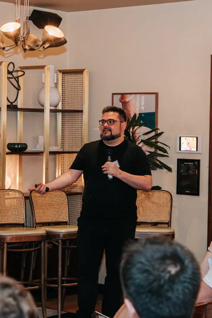 A speaker holding a microphone and gesturing to attendees at the July gathering